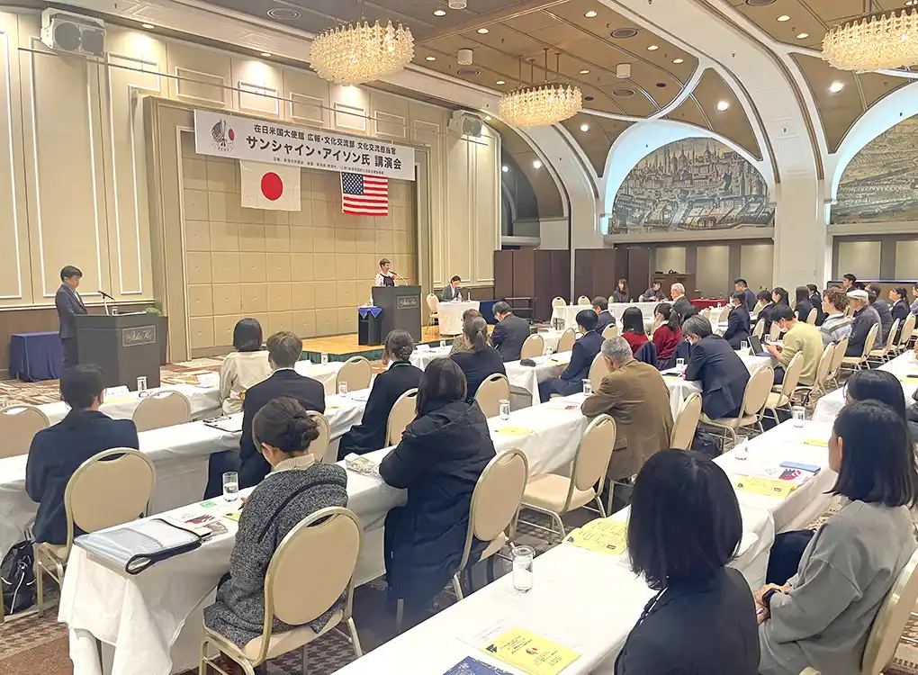 Seminar-style international exchange event with attendees listening to a keynote speaker
