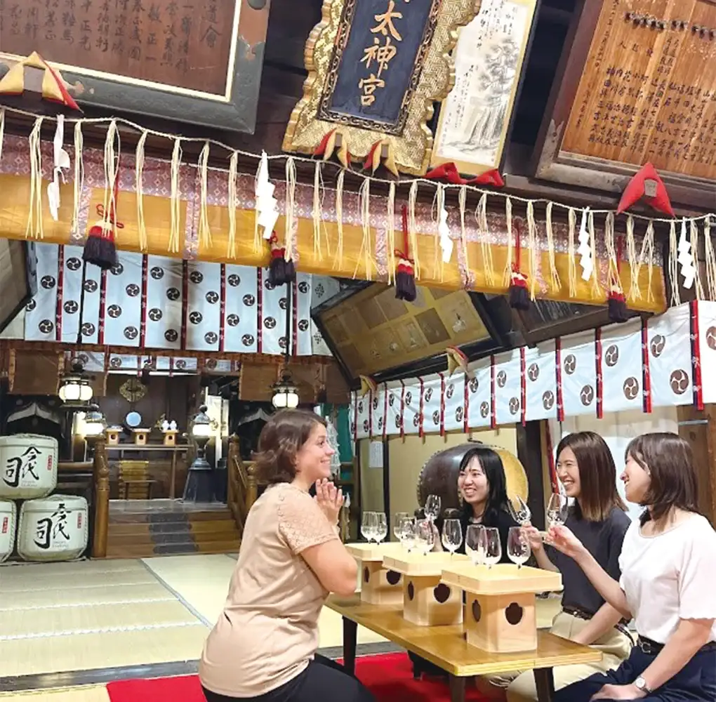 Group of women enjoying sake tasting inside a traditional Japanese shrine with wooden interior and lanterns