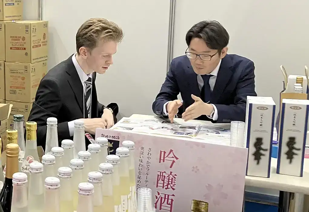 Japanese businessman discussing products with a foreign buyer at a sake trade fair booth